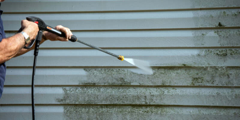 power wash siding on home with power washer holding nozzle at safe distance and angle